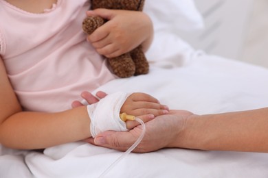 Photo of Mother and her little daughter with IV drip on bed in hospital, closeup