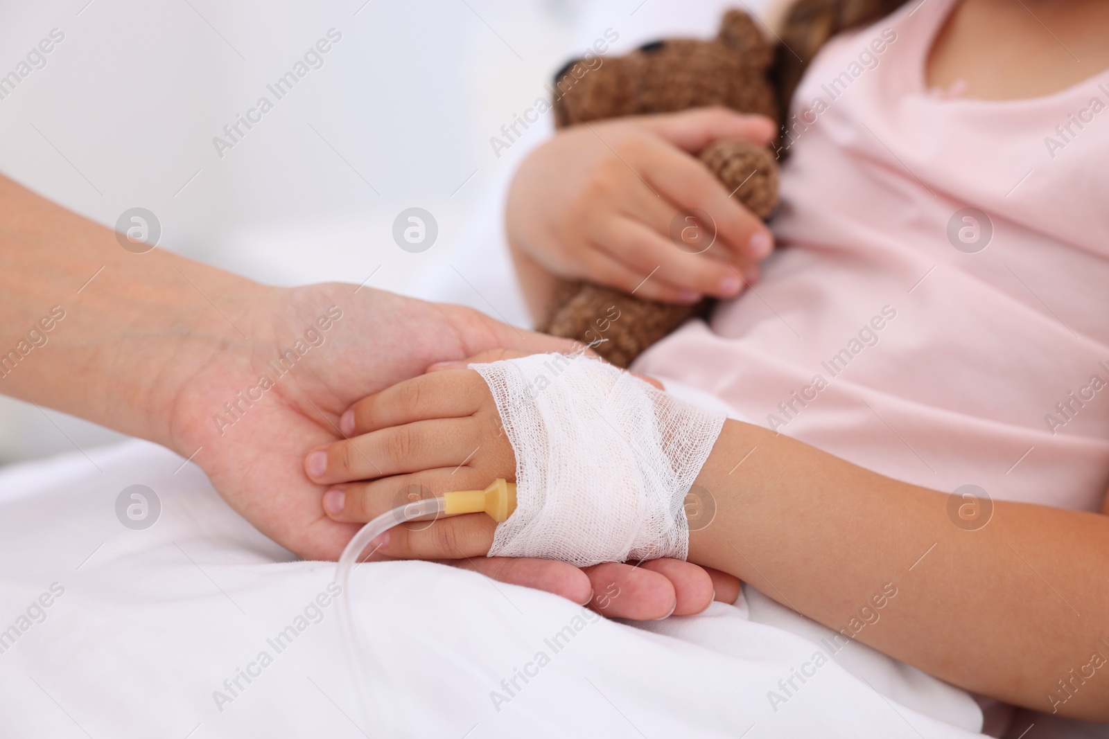 Photo of Mother and her little daughter with IV drip on bed in hospital, closeup