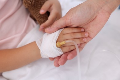 Photo of Mother and her little daughter with IV drip on bed in hospital, closeup