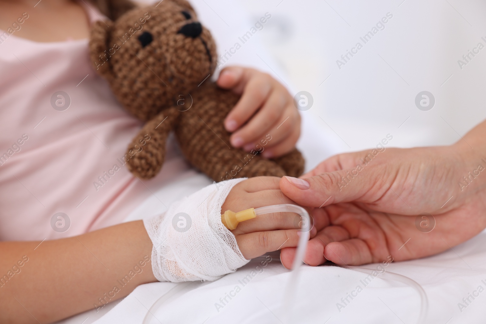 Photo of Mother and her little daughter with IV drip on bed in hospital, closeup