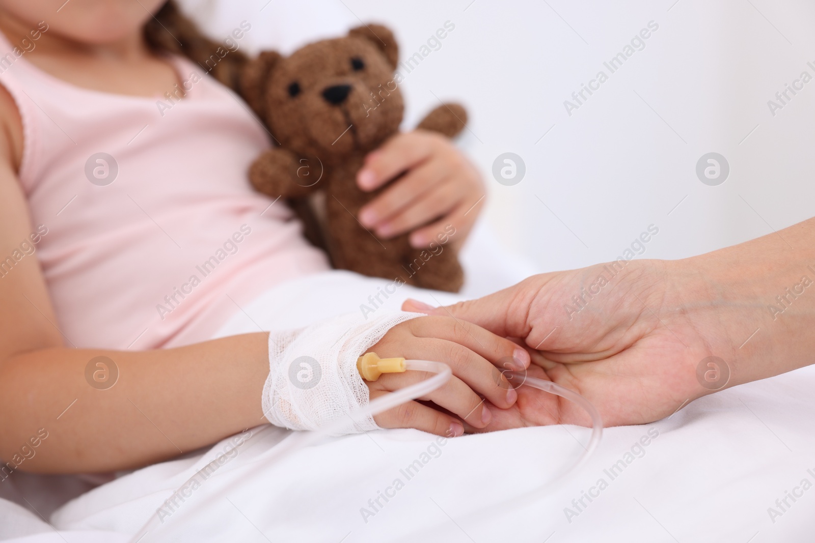 Photo of Mother and her little daughter with IV drip on bed in hospital, closeup