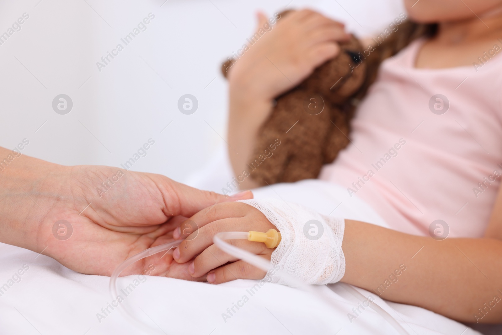 Photo of Mother and her little daughter with IV drip on bed in hospital, closeup