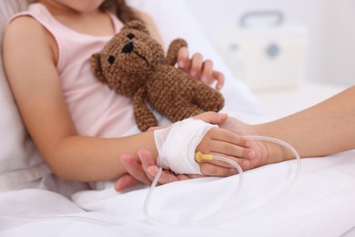 Photo of Mother and her little daughter with IV drip on bed in hospital, closeup