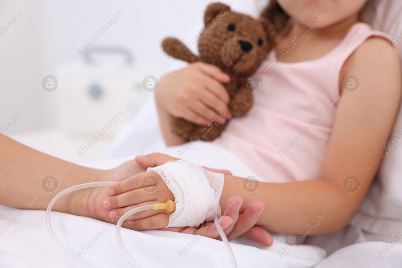 Photo of Mother and her little daughter with IV drip on bed in hospital, closeup