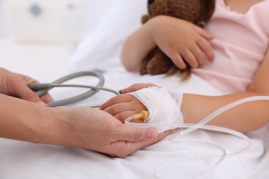 Photo of Doctor examining little girl and setting IV drip on bed at hospital, closeup