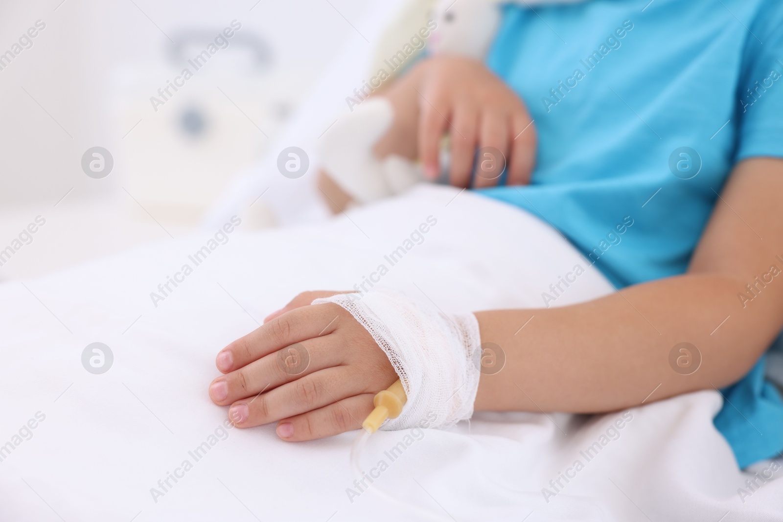 Photo of Little girl with IV drip on bed in hospital, closeup