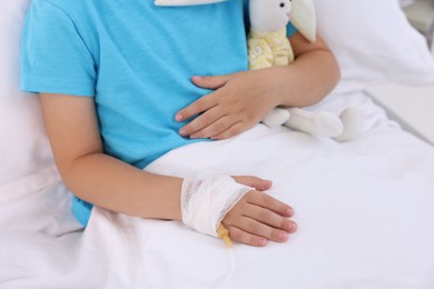 Photo of Little girl with IV drip on bed in hospital, closeup