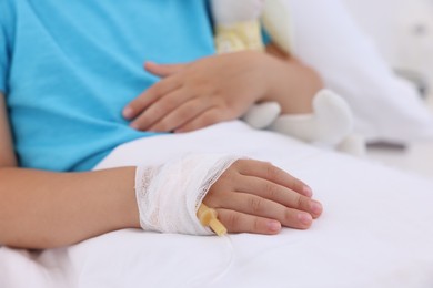 Little girl with IV drip on bed in hospital, closeup