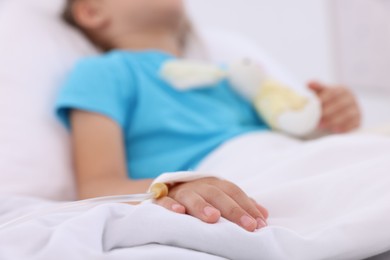 Photo of Little girl with IV drip on bed in hospital, closeup