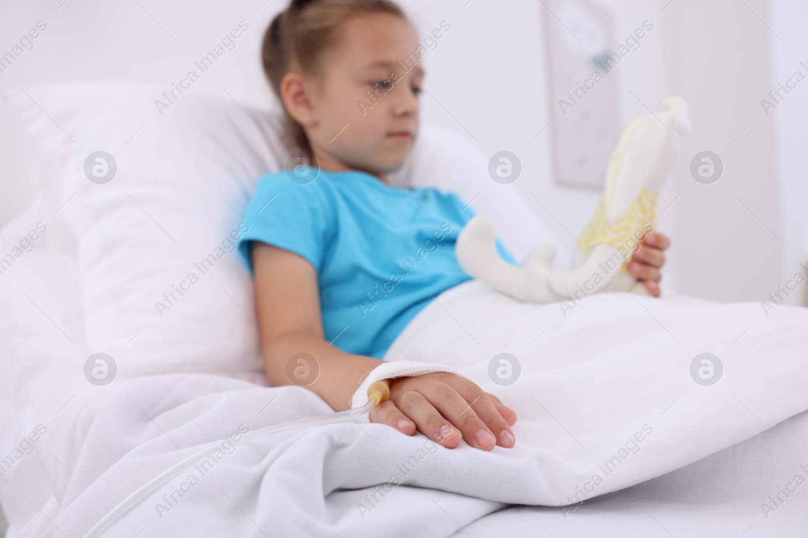 Photo of Little girl with IV drip on bed in hospital, selective focus