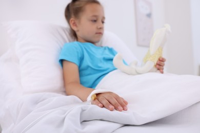 Little girl with IV drip on bed in hospital, selective focus