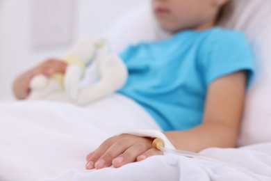 Photo of Little girl with IV drip on bed in hospital, closeup