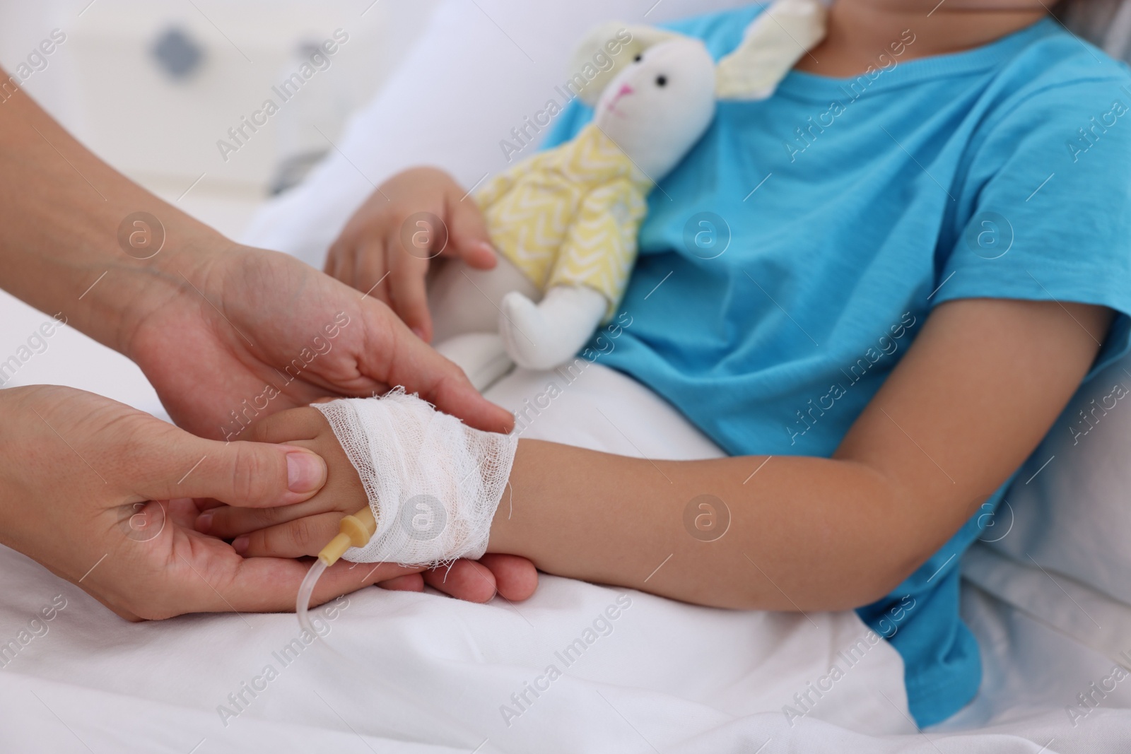 Photo of Doctor examining little girl and setting IV drip on bed at hospital, closeup