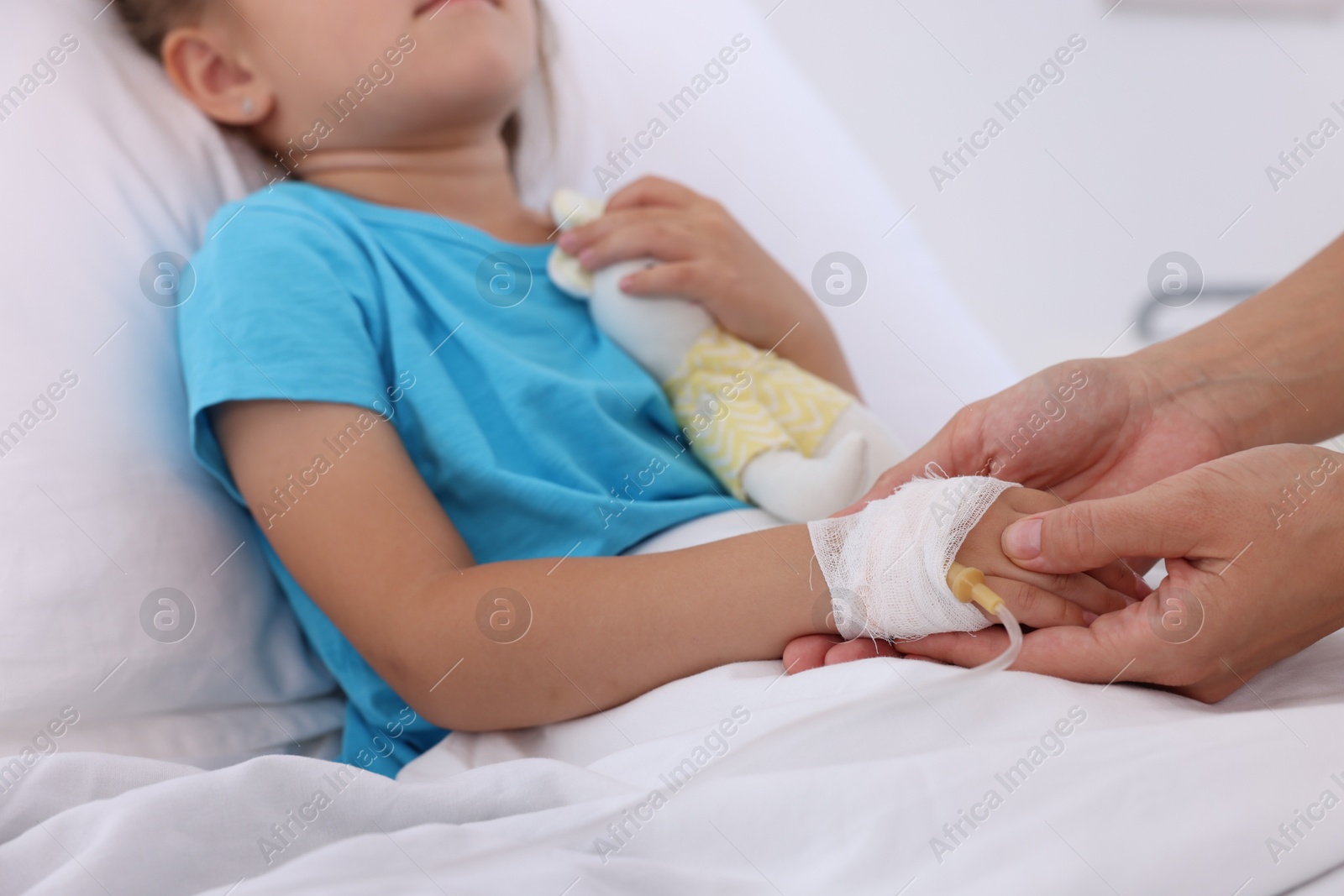 Photo of Doctor examining little girl and setting IV drip on bed at hospital, closeup