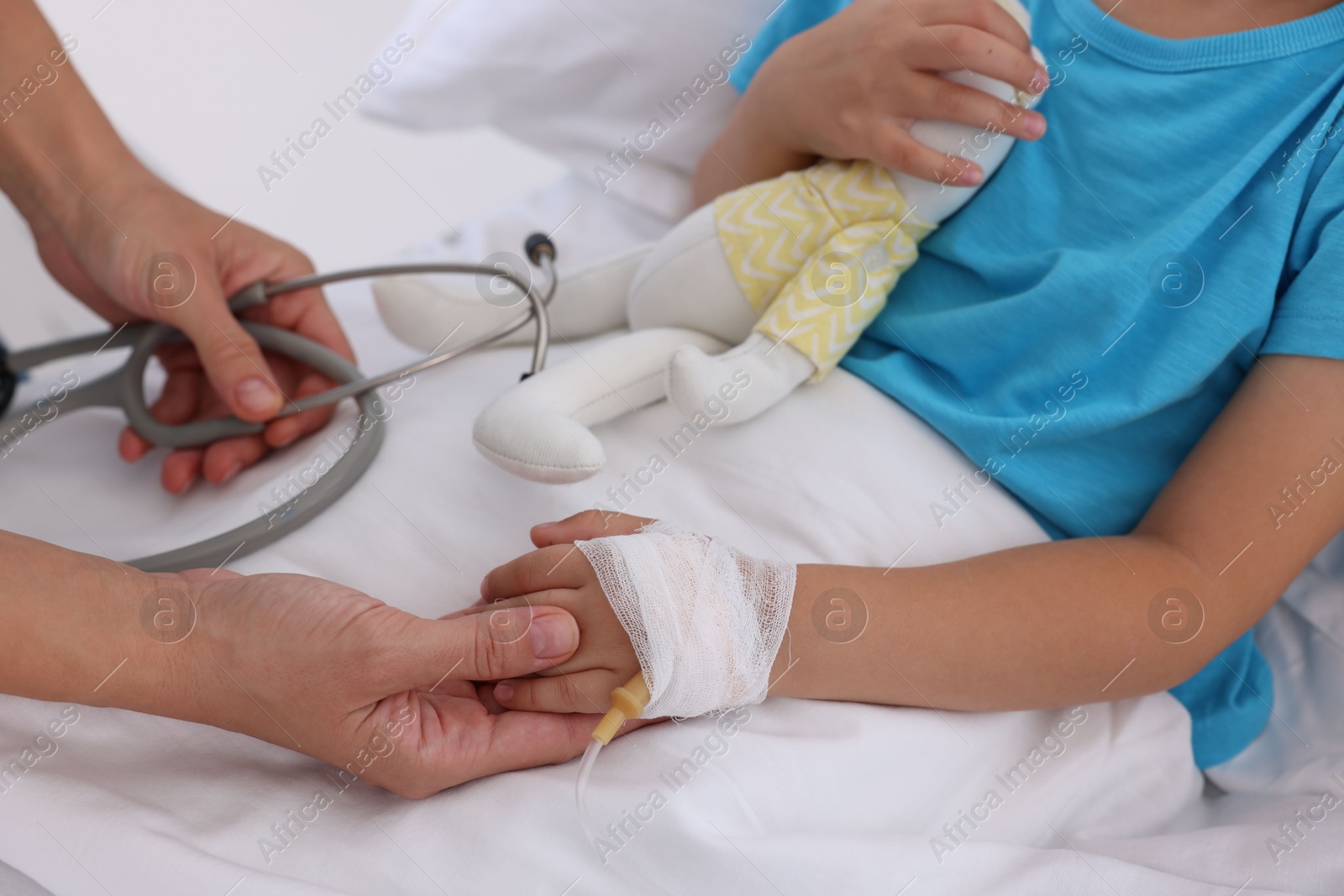 Photo of Doctor examining little girl and setting IV drip on bed at hospital, closeup