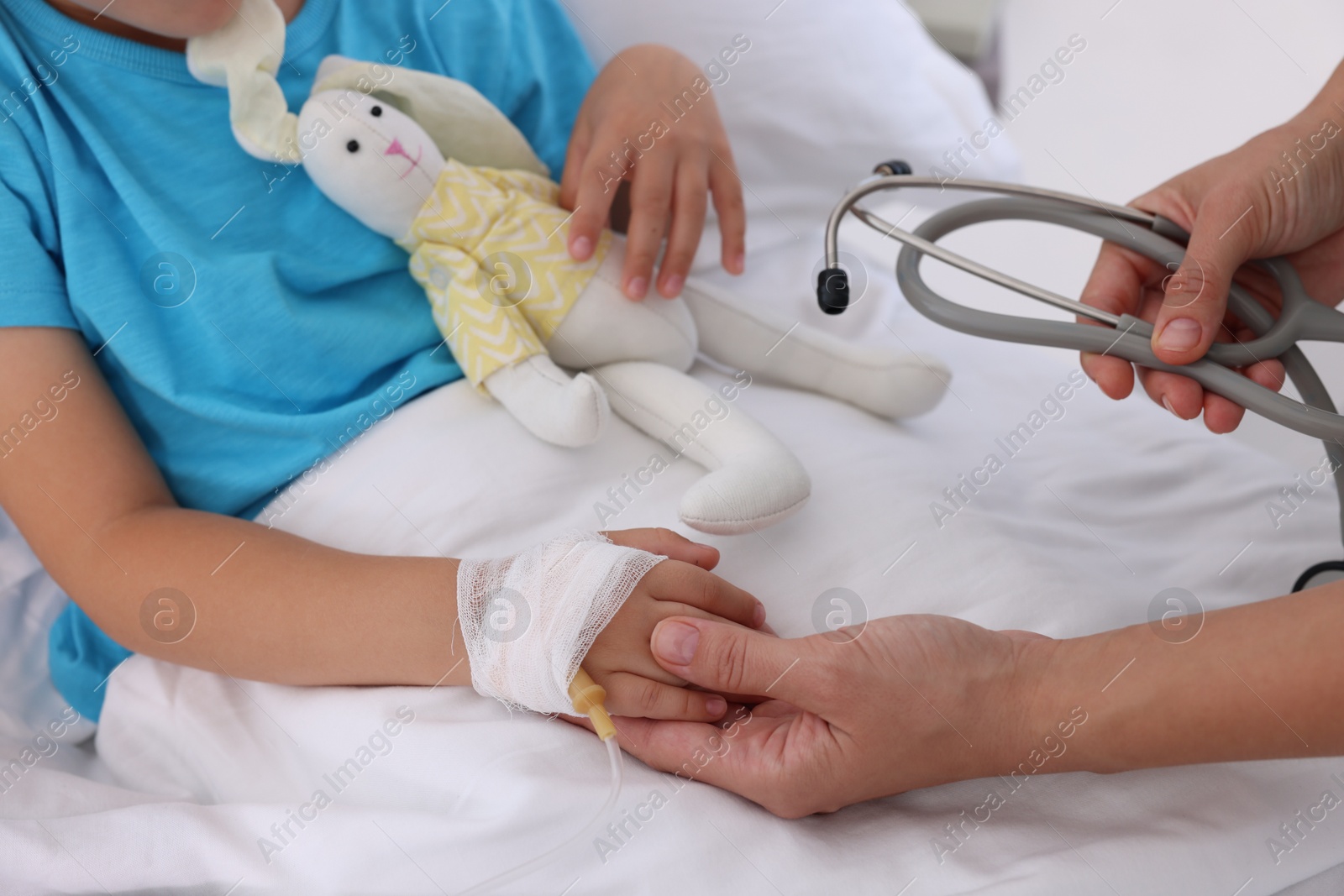 Photo of Doctor examining little girl and setting IV drip on bed at hospital, closeup