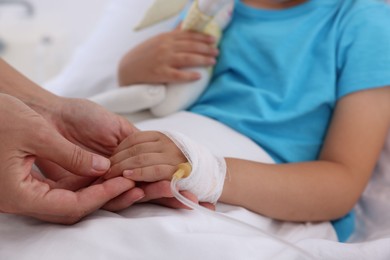 Photo of Doctor examining little girl and setting IV drip on bed at hospital, closeup