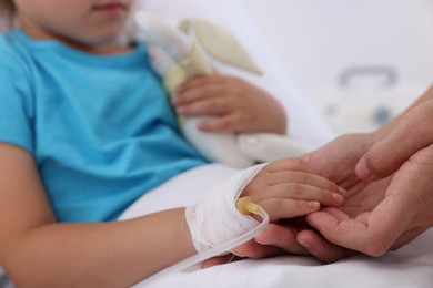 Photo of Doctor examining little girl and setting IV drip on bed at hospital, closeup