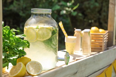 Photo of Lemonade stand with refreshing drink, fresh fruits and mint in park