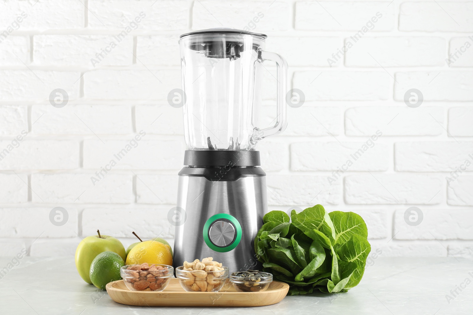 Photo of Blender and products on light table against white brick wall