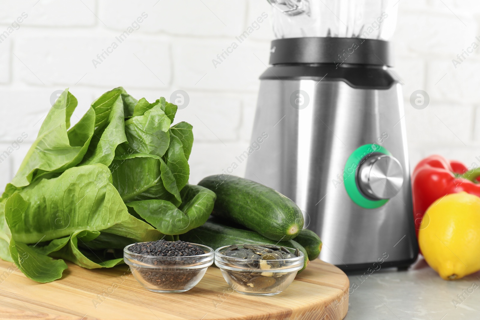 Photo of Healthy products and blender on grey table against white brick wall, closeup