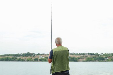 Photo of Fisherman with rod fishing near lake at summer, back view