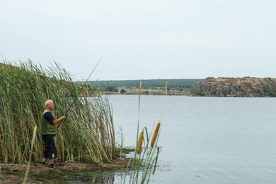 Photo of Fisherman with rod fishing near lake at summer