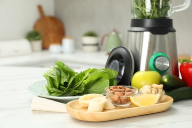 Photo of Modern blender with ingredients for smoothie on white marble table in kitchen, closeup