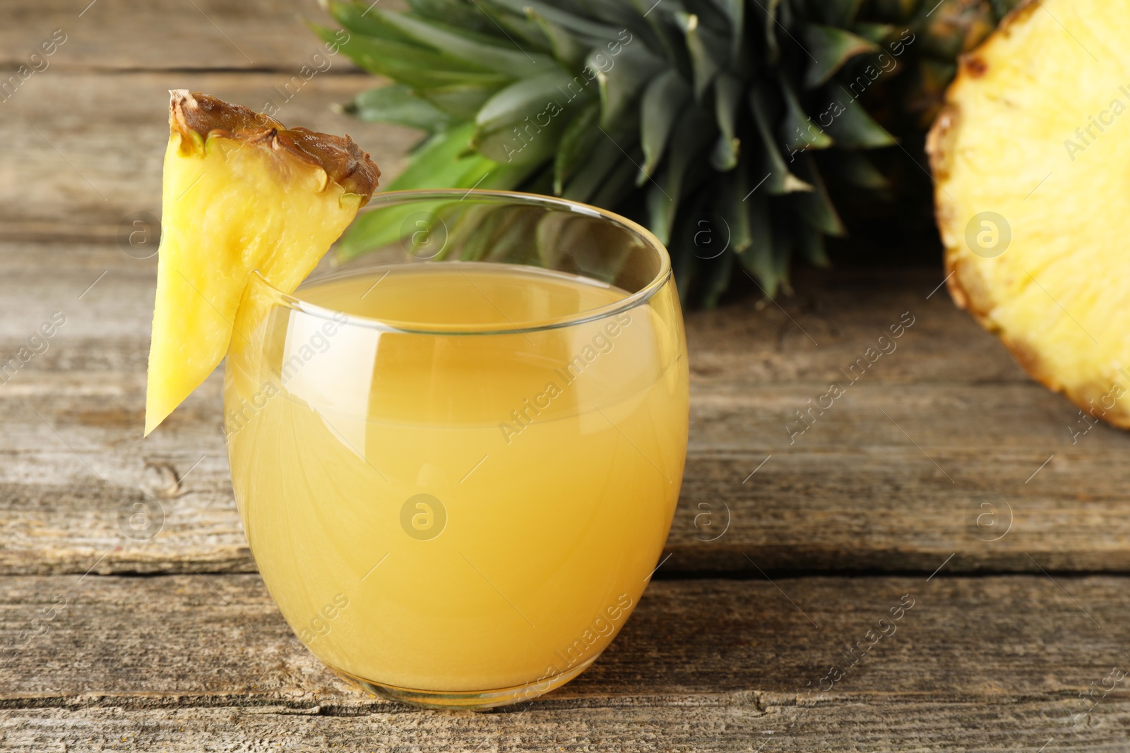 Photo of Tasty pineapple juice in glass and fresh fruit on wooden table, closeup