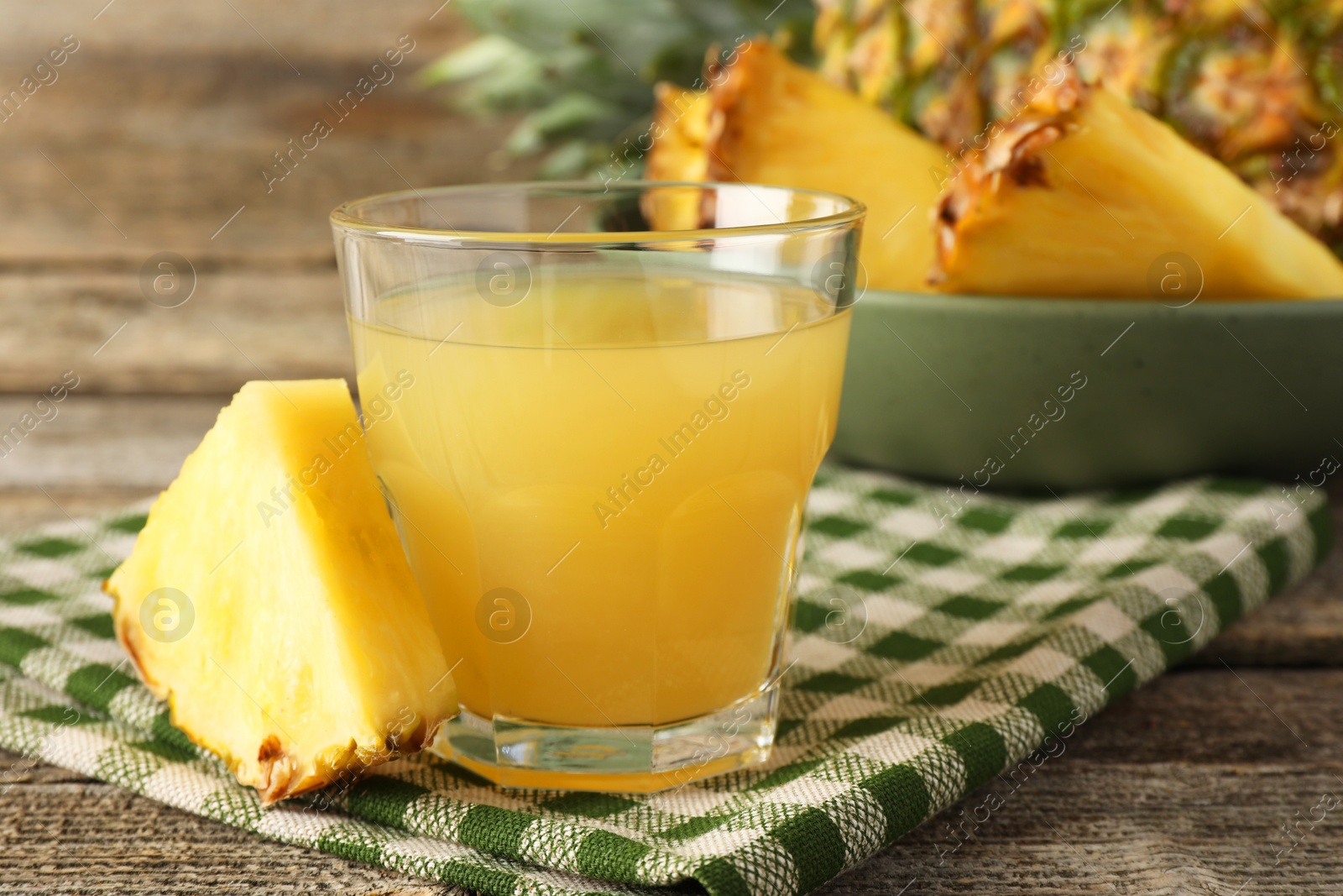 Photo of Tasty pineapple juice in glass and slice of fresh fruit on wooden table, closeup