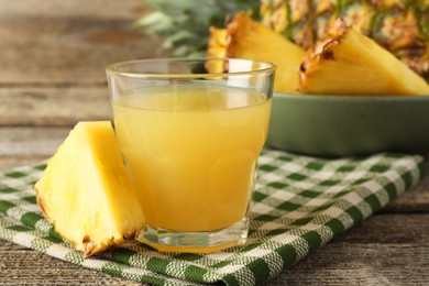 Photo of Tasty pineapple juice in glass and slice of fresh fruit on wooden table, closeup