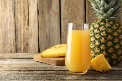 Photo of Tasty pineapple juice in glass and fresh fruits on wooden table, closeup. Space for text