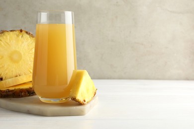 Photo of Tasty pineapple juice in glass and slices of fresh fruit on white wooden table against grey background, closeup. Space for text