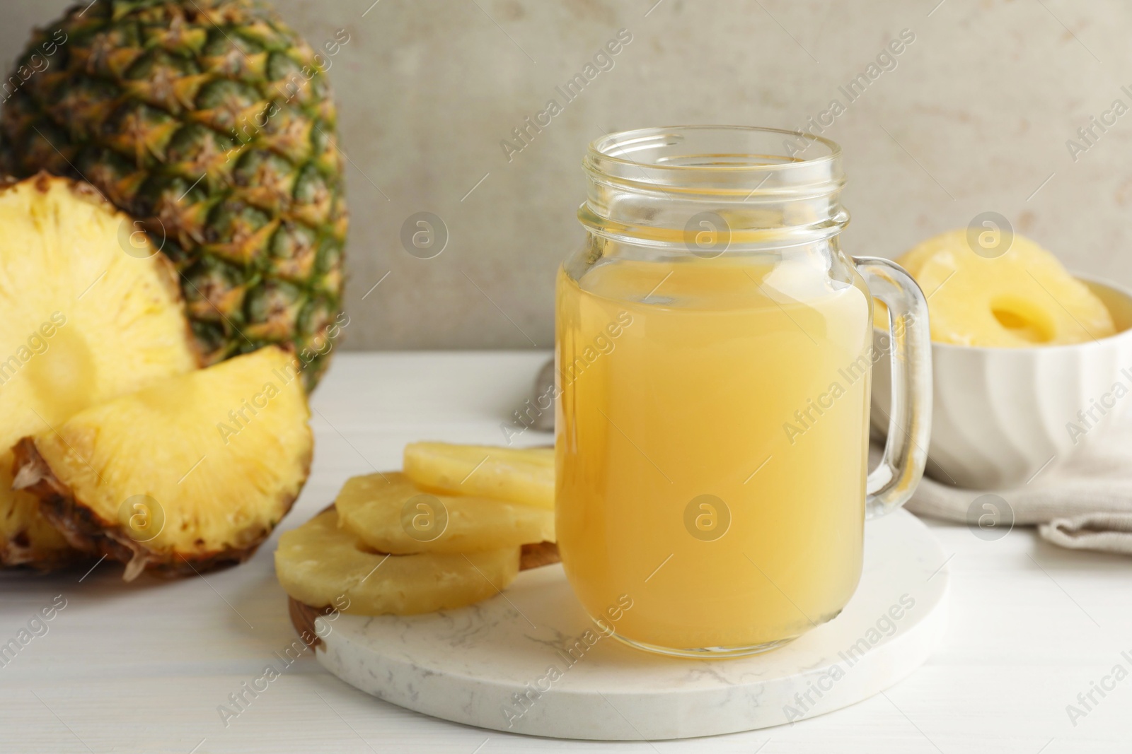 Photo of Tasty pineapple juice in mason jar and fresh fruits on white wooden table against grey background, closeup