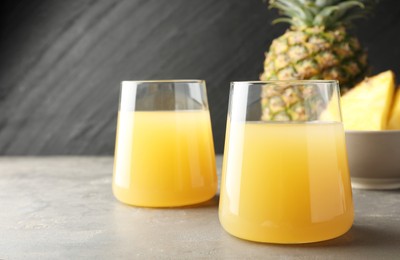 Photo of Tasty pineapple juice in glasses and fruits on grey textured table, closeup