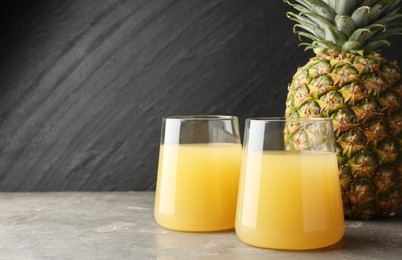 Photo of Tasty pineapple juice in glasses and fruit on grey textured table. Space for text