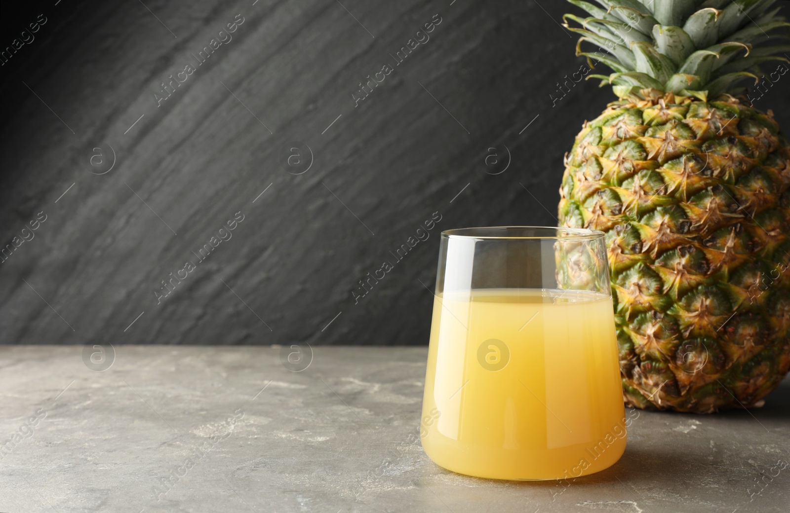 Photo of Tasty pineapple juice in glass and fruit on grey textured table. Space for text