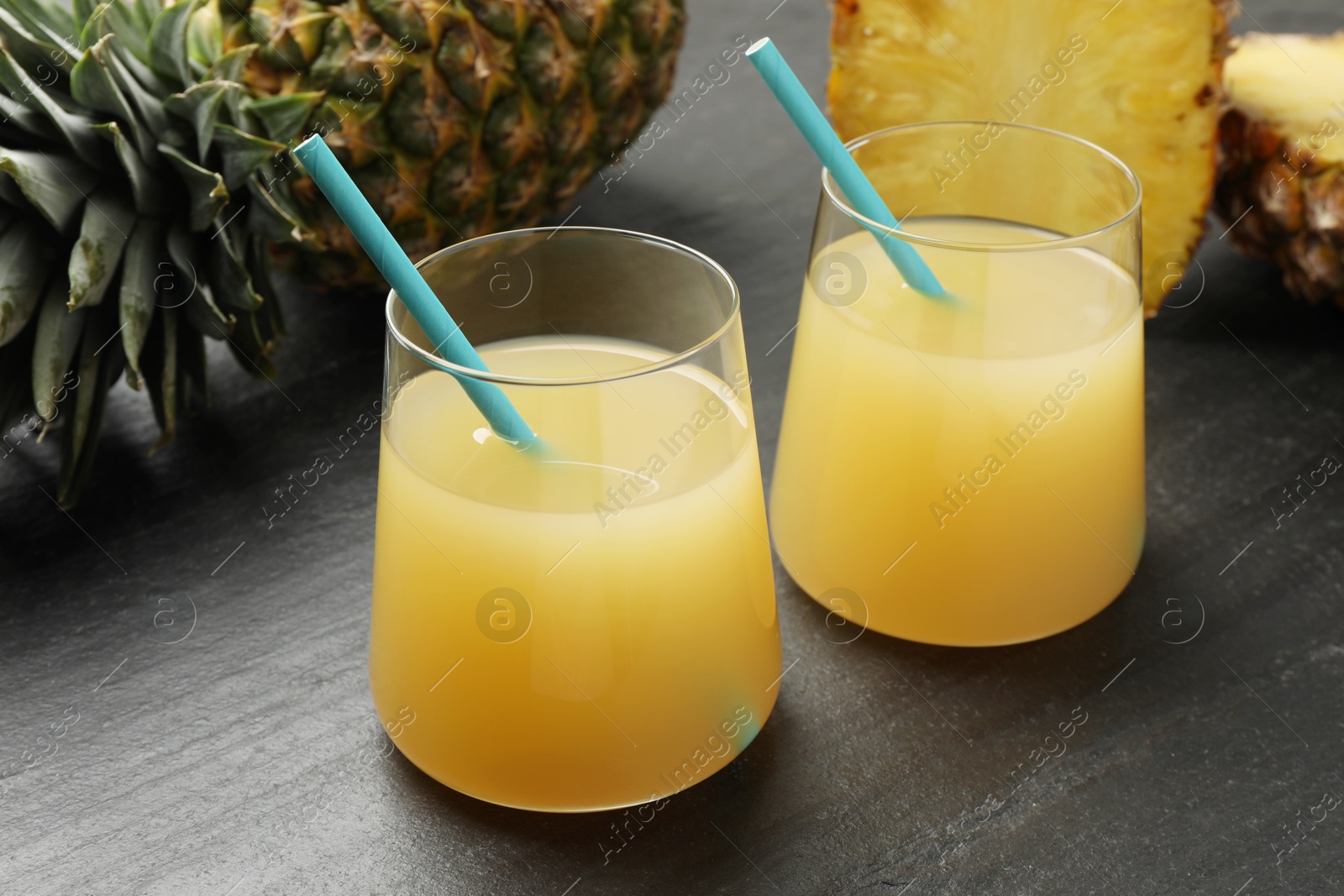 Photo of Tasty pineapple juice in glasses and fruits on grey textured table, closeup