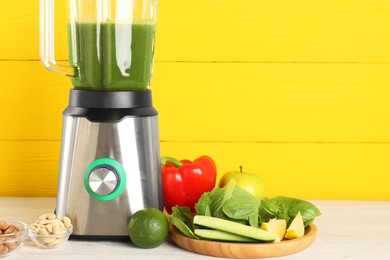 Modern blender with smoothie and ingredients on light wooden table. Space for text