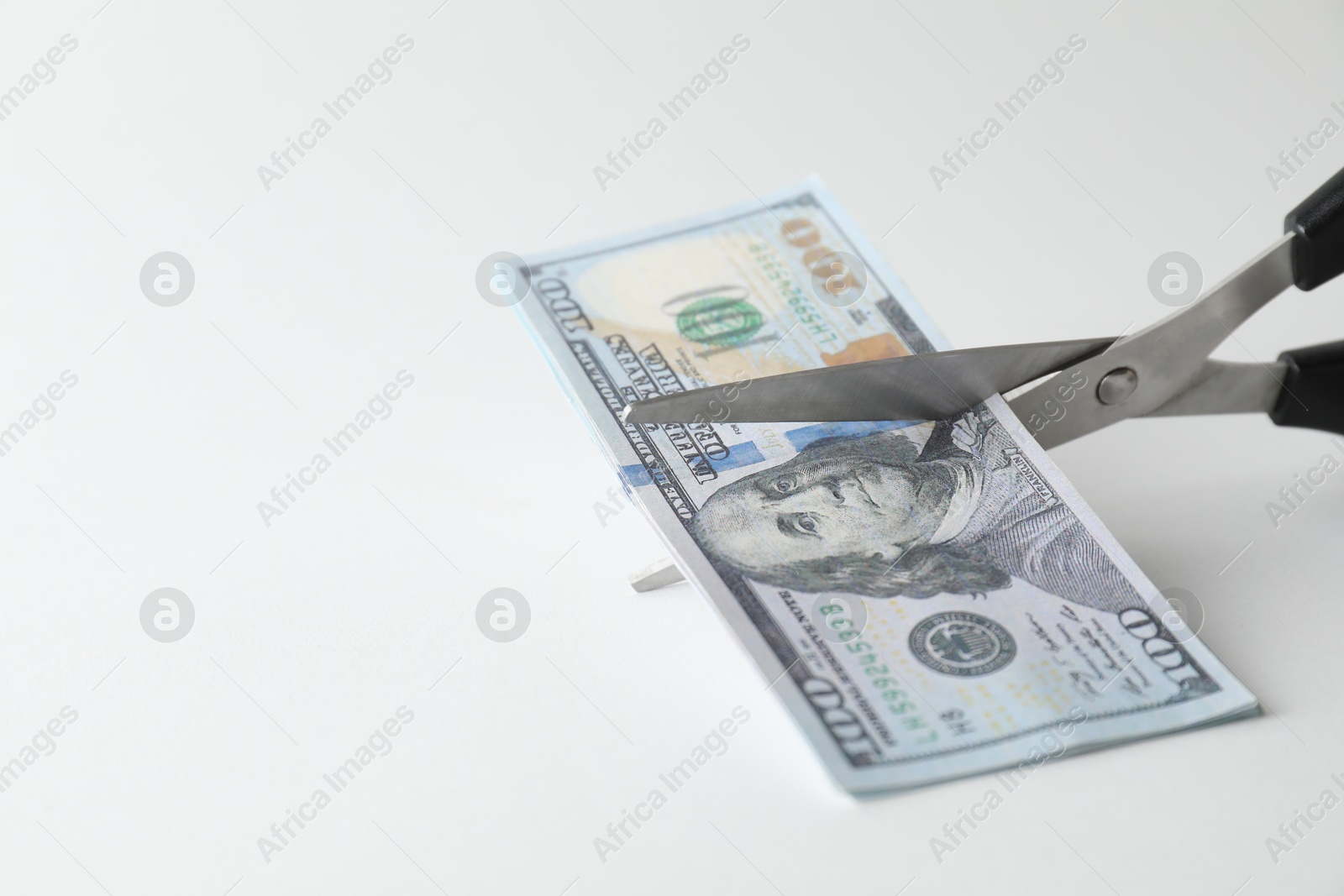 Photo of Budgeting. Cutting dollar banknotes with scissors on white background, closeup. Space for text