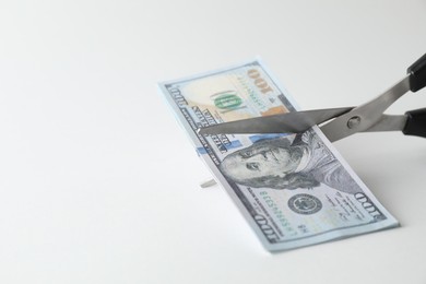 Photo of Budgeting. Cutting dollar banknotes with scissors on white background, closeup. Space for text