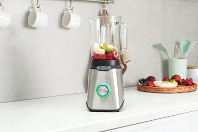 Blender and fresh ingredients on white marble countertop in kitchen, space for text