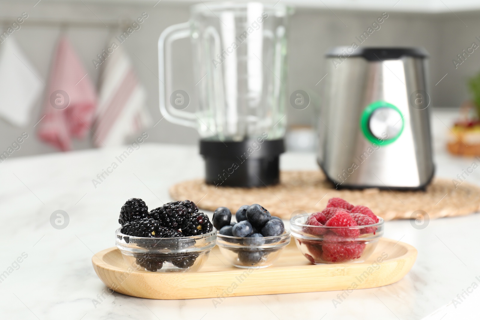 Photo of Blender kit and fresh berries on white marble table, selective focus