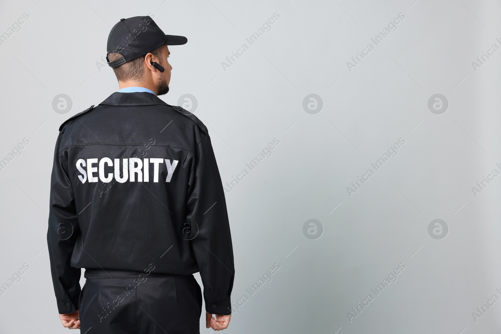 Photo of Security guard in uniform with earpiece on grey background, back view. Space for text