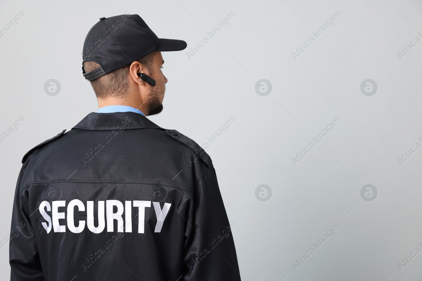 Photo of Security guard in uniform with earpiece on grey background, back view. Space for text