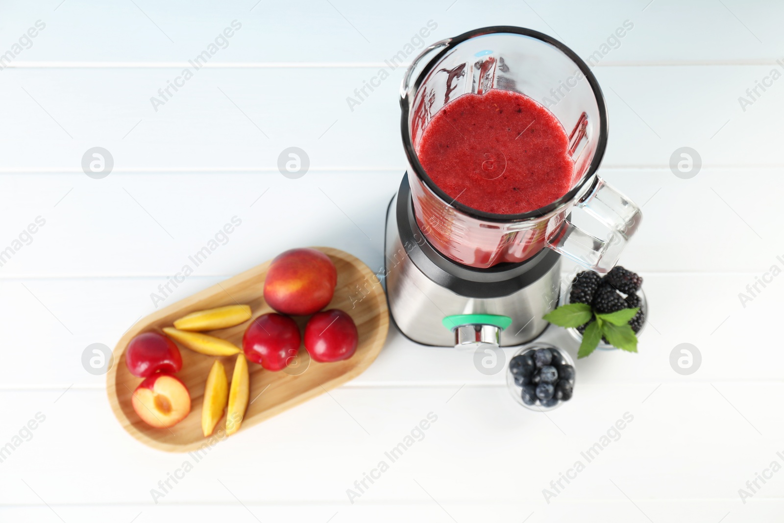 Photo of Blender with mixture of ingredients and other fresh products on white wooden table, above view