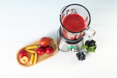 Blender with mixture of ingredients and other fresh products on white wooden table, above view