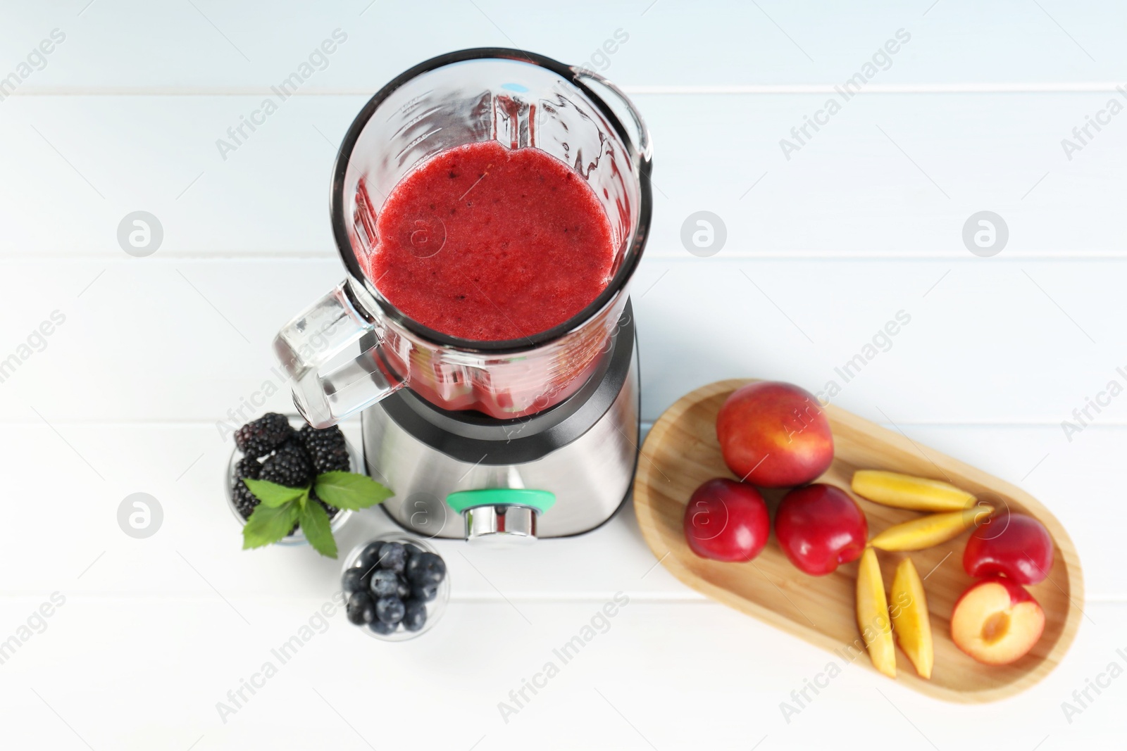 Photo of Blender with mixture of ingredients and other fresh products on white wooden table, above view