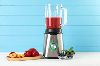 Photo of Blender with mixture of ingredients and other fresh products on white wooden table