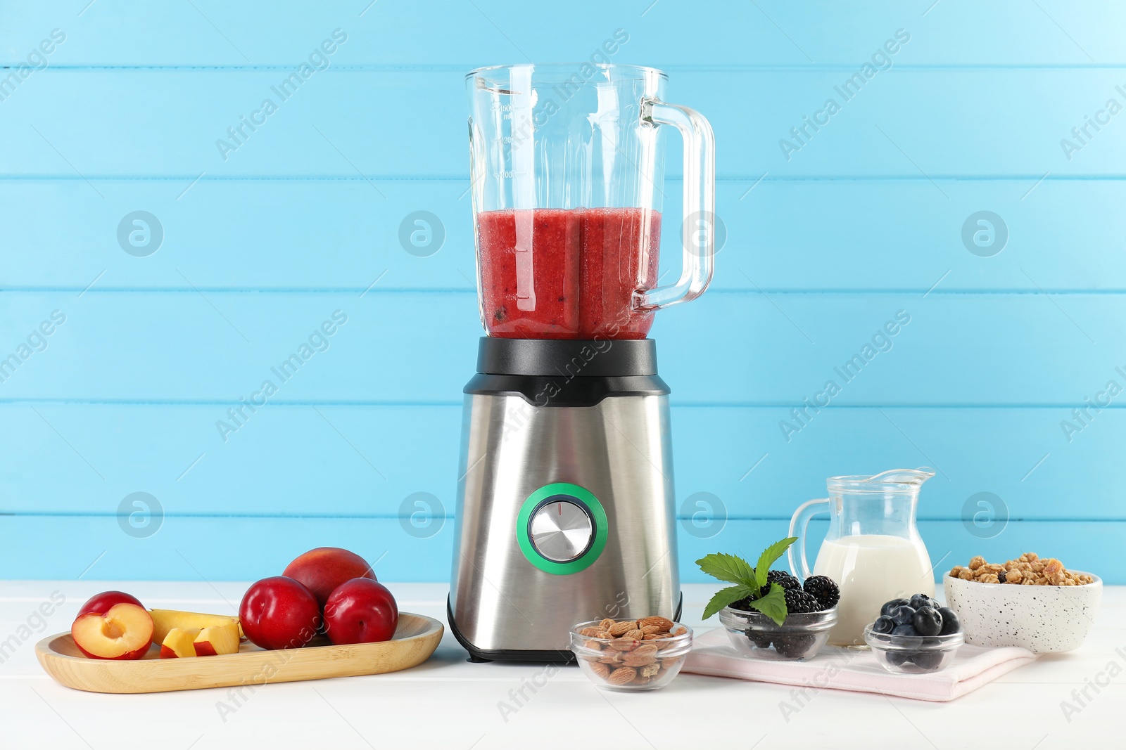 Photo of Blender with mixture of ingredients and other fresh products on white wooden table